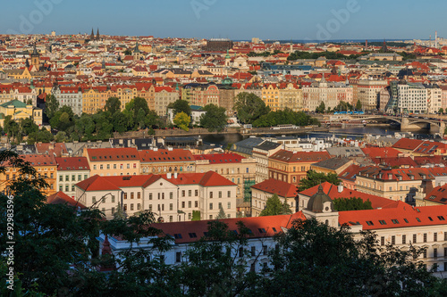 View over the roofs and historical buildings of Prague the capital of the Czech Republic on a sunny day with blues sky and bushes in the foreground © Marco