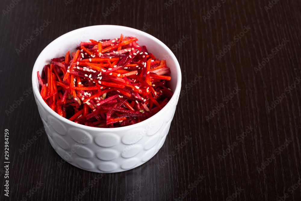 Vegetable salad of apple, carrot and beetroot with lemon juice, sesame seeds and vegetable oil in a white deep plate