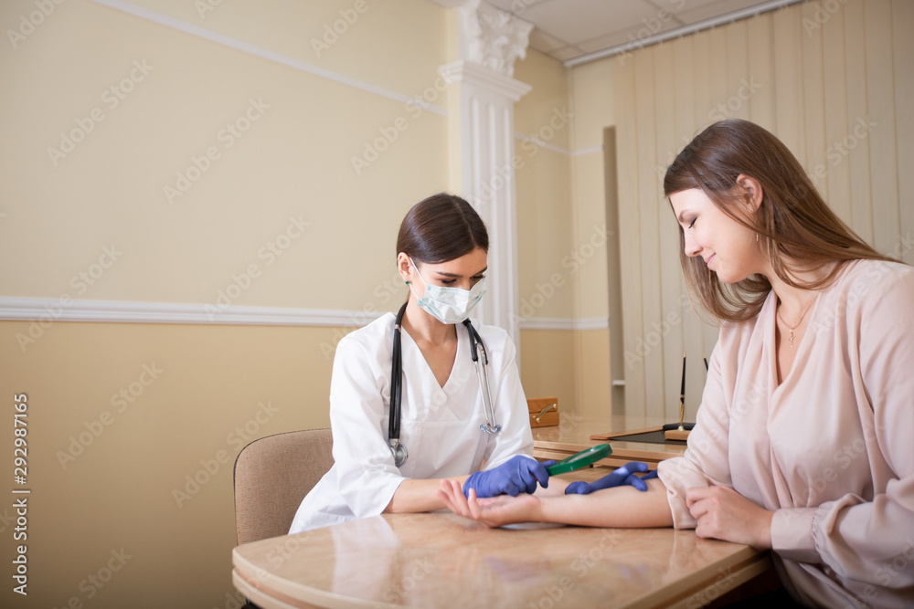 Fototapeta premium Dermatologist examines a patient's mole on the arm with a magnifying glass in the clinic