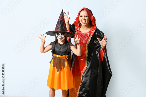 Mother with little daughter in Halloween costumes on light background