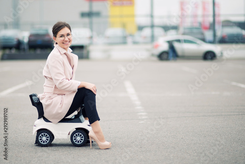 young woman sits on a children's plastic car