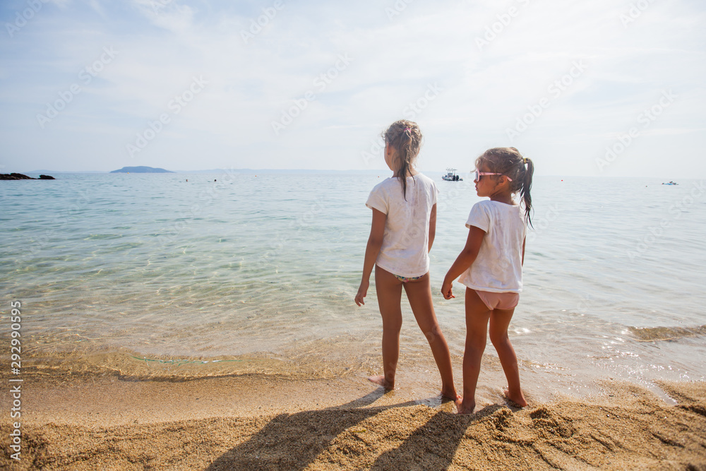 Two little girls standing together on the sand beach