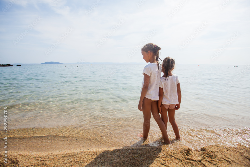 Two little girls standing together on the sand beach Two little girls standing together on the sand beach