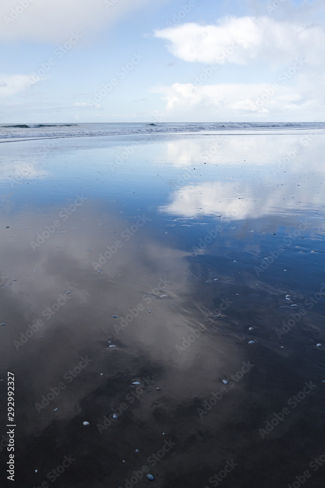 Obraz premium Coastline of \new Zealand, showing the reflection of sun and clouds in the water and sand. 