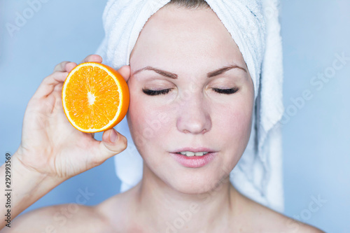 The natural beauty of a woman. Girl with a towel on her head after the procedure, an orange in her hands near her face. Care for the radiant skin of the face and fresh skin of the girl. Beautiful