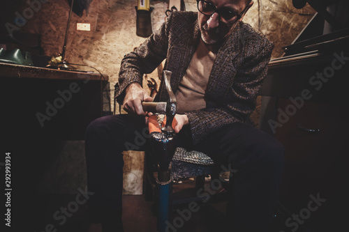 Focused mature cobbler is fixing sole for boots using hammer.