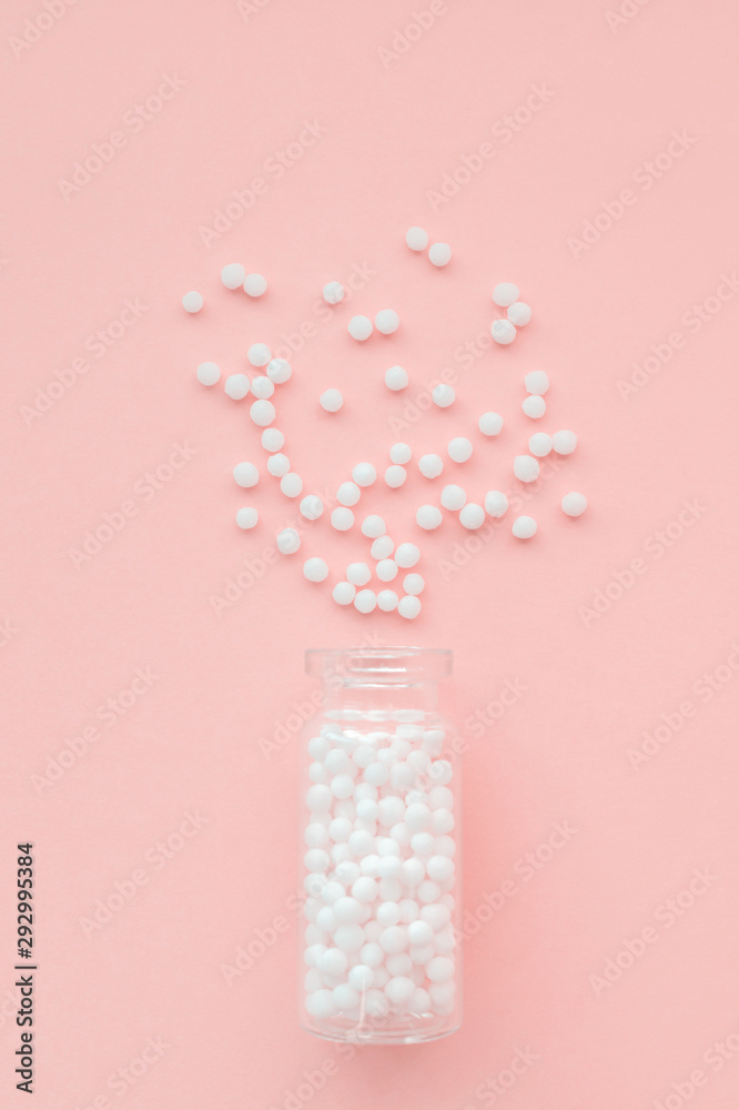 Homeopathic globules in glass bottle on pastel pink background. The globules are scattered from bottle. Alternative homeopathy medicine herbs, healthcare and pills concept. Selective focus Homeopathic globules in glass bottle on pastel pink background. The globules are scattered from bottle. Alternative homeopathy medicine herbs, healthcare and pills concept. Selective focus