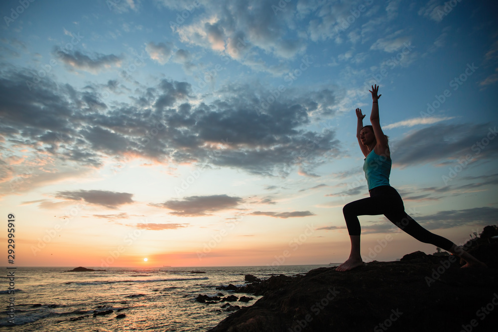Fototapeta premium Young fitness woman sees off the sun on the ocean coast. Exercises, yoga and training. .