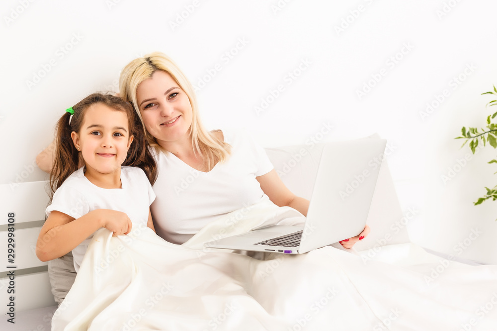 Smiling mother and daughter using laptop in bed at home