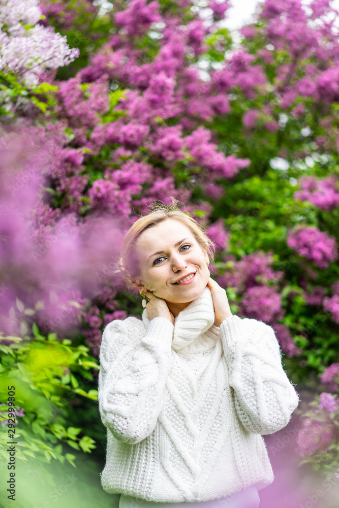 Beautiful blond woman posing outdoors at the blur spring park of violet and white lilac background