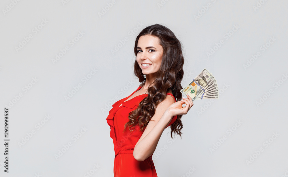 Portrait of happy beautiful brunette young woman in red dress holding dollars money. Gray background. Sale, finance, banking, winning, economic, credit, business, shopping concept. USD Portrait of happy beautiful brunette young woman in red dress holding dollars money. Gray background. Sale, finance, banking, winning, economic, credit, business, shopping concept. USD