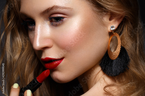 Beautiful girl with red lips and classic makeup and curls with lipstick in hand. Beauty face