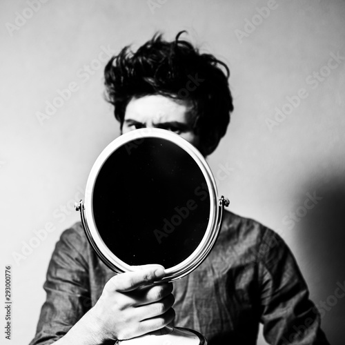Fotografia Black and white portrait of young guy with small mirror in hand.