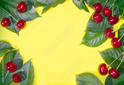 Frame of red ripe cherries on a yellow background.