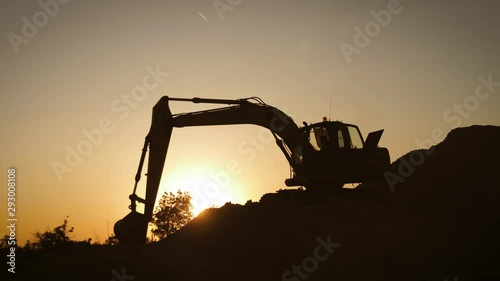 Silhouette of an excavator that loads sand into a truck at sunset. Concept construction and heavy industry, machine will be used in heavy industry business. Slow motion footage. photo