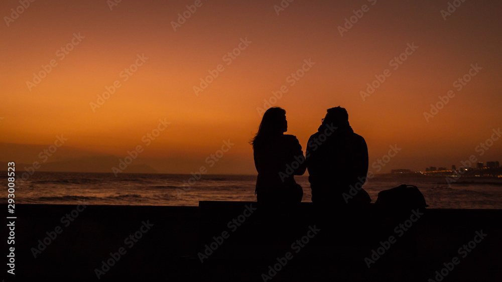 A woman and a man looking the sunset in the sea.