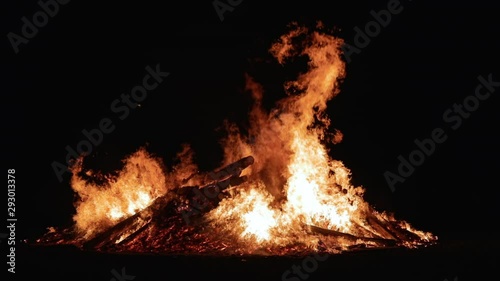 A large crowd of people celebrate an ethnic holiday by a giant bonfire. Burning red hot sparks rise from large fire in the night sky. Belarusian Kupalle. Russian ethnic holiday Ivan Kupala in village. photo