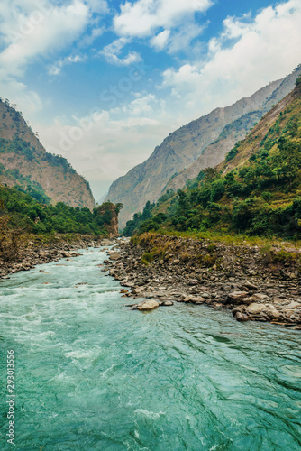 River flows trough rocky valley in Himalaya mountains in Nepal during sunny summer day.	