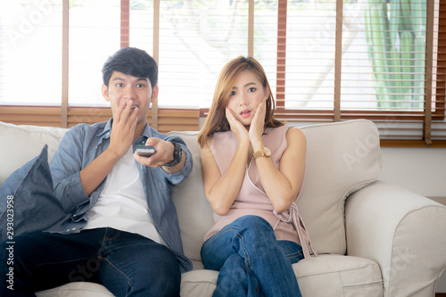 Young asian couple watching horror movie with relax and enjoy holding remote control tv at home, asia man and woman fun surprised and scared together at home, entertainment concept.