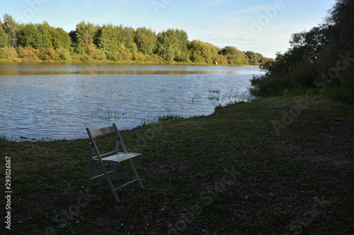 Summer landscape with a river and a white chair in the foreground.