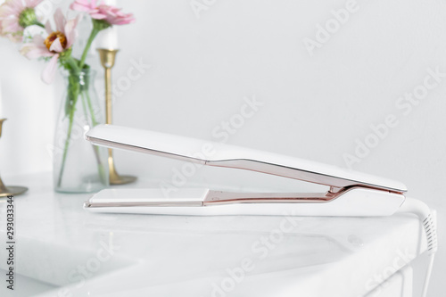 Modern hair straightener on white marble countertop, brass decor with candles and flowers, bobby pins, girly bathroom, copy space photo