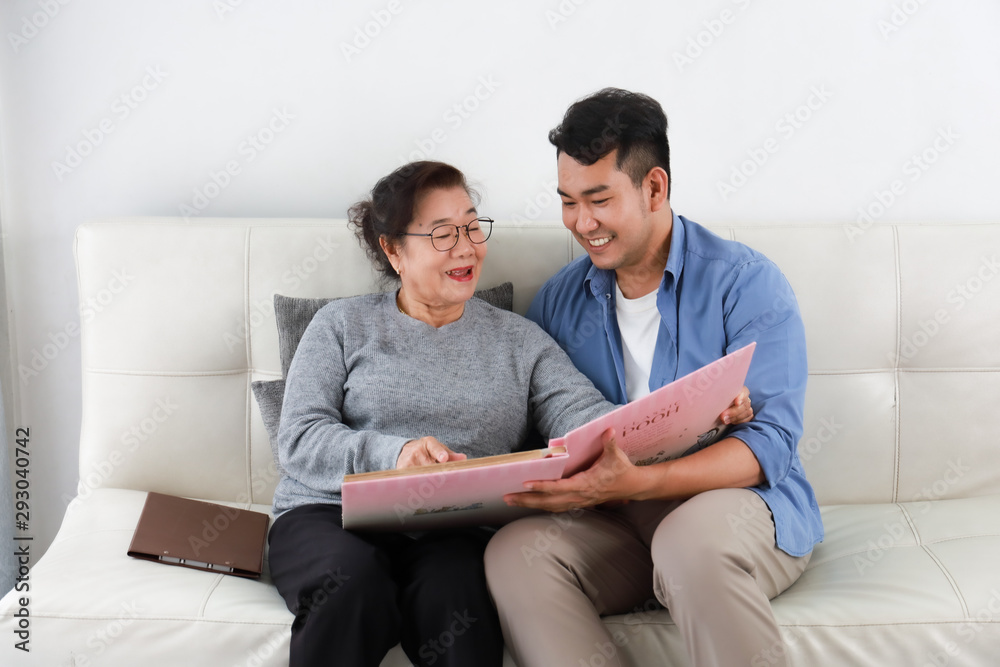 Asian senior woman mother and young man son in blue shirt looking photo album and talking happy smile face  in living room