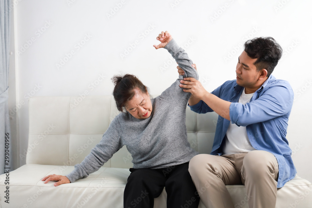 Asian senior woman mother and young man son in blue shirt massage his mother in living room Asian senior woman mother and young man son in blue shirt massage his mother in living room