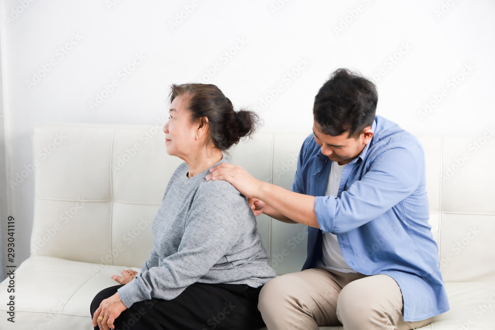 Asian senior woman mother and young man son in blue shirt massage his mother in living room Asian senior woman mother and young man son in blue shirt massage his mother in living room