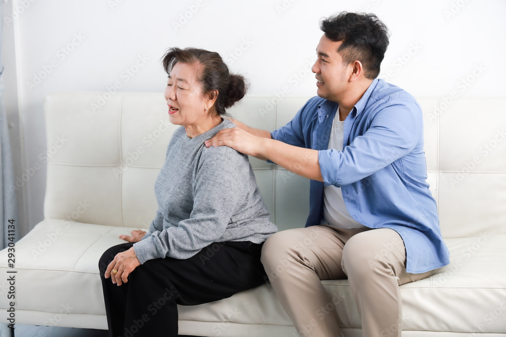 Asian senior woman mother and young man son in blue shirt massage his mother in living room Asian senior woman mother and young man son in blue shirt massage his mother in living room