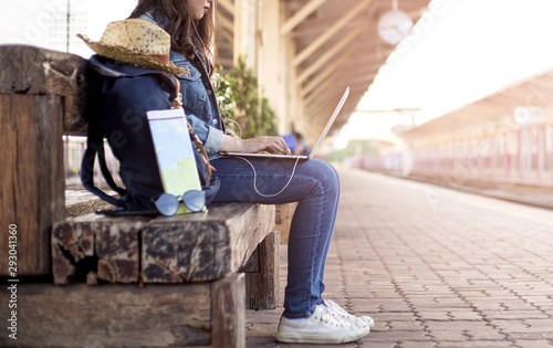 Summer day of Asian woman sitting using laptop at train station. She have camera film, Backpack, hat, map and smartphone. Travel and work freelance concept. hipster style.