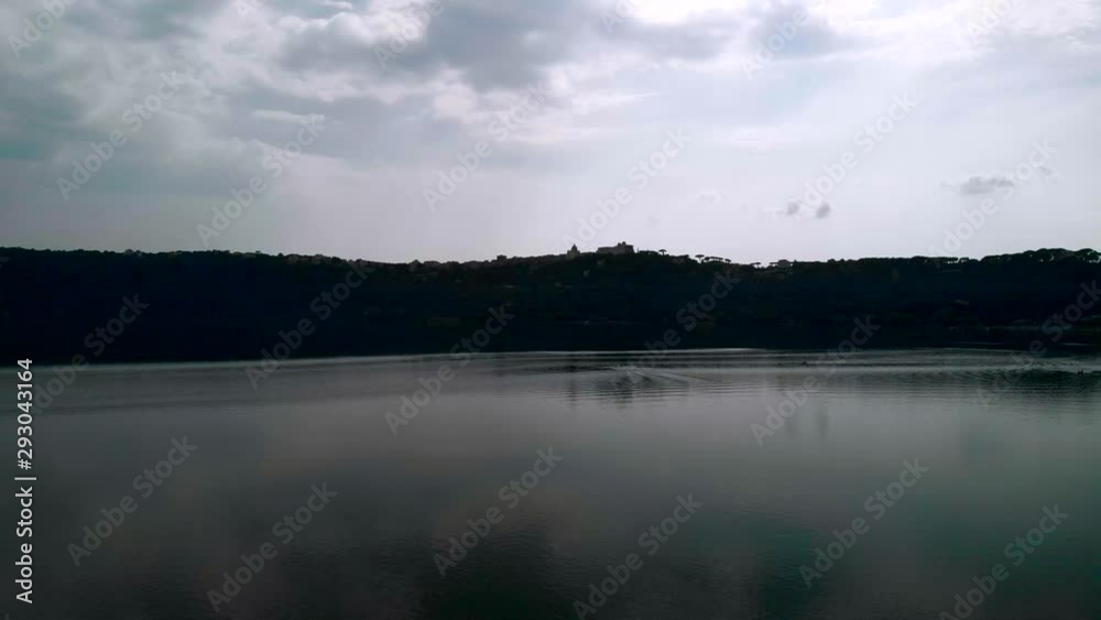 AERIAL TRUCK RIGHT: Drone flying over Lake Albano in Rome, Italy with stunning trees' reflection on the water and a papal summer residence in the distance AERIAL TRUCK RIGHT: Drone flying over Lake Albano in Rome, Italy with stunning trees' reflection on the water and a papal summer residence in the distance
