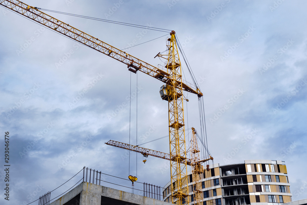 One high-rise crane against a house and sky during the construction phase. Mortgage, business, real estate loan. Cloudy.