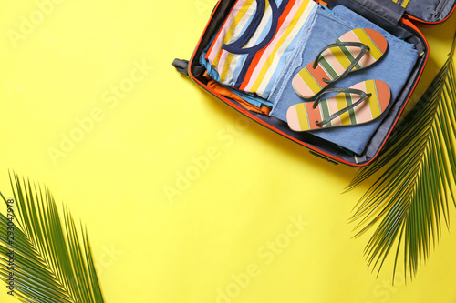 Open suitcase and beach accessories on yellow background  flat lay. Space for text