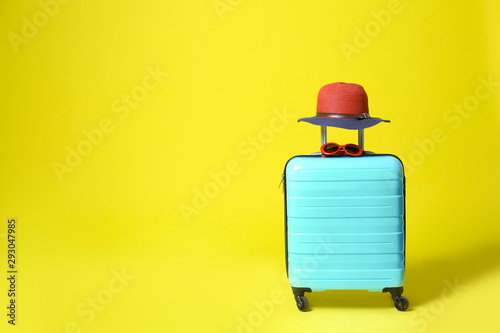 Stylish blue suitcase with hat and sunglasses on yellow background. Space for text