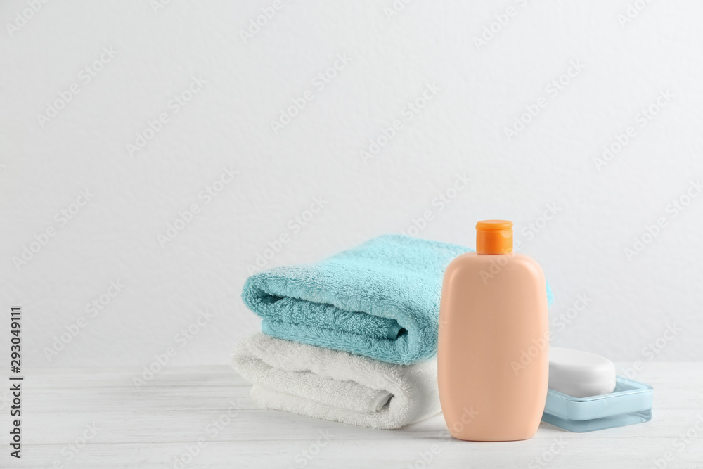 Fresh towels and bottle of cosmetic product on white wooden table. Space for text