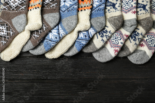 Different knitted socks on black wooden background, flat lay