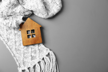 Wooden house model and scarf on grey background, top view with space for text. Heating efficiency