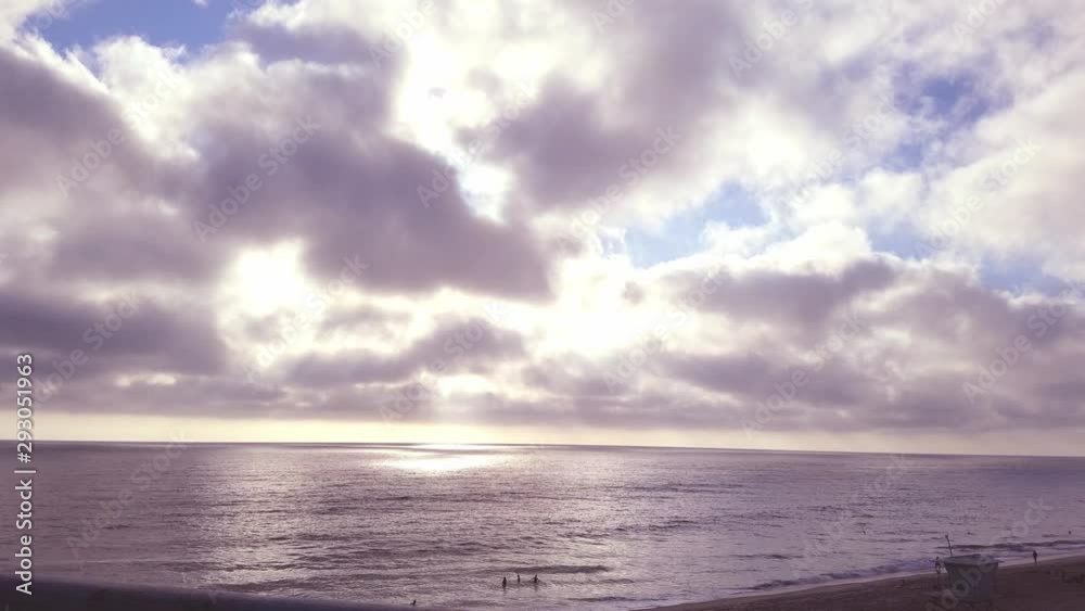 People play in the ocean as dramatic clouds at sunset cast strong contrasting shadows as the sun breaks through. People play in the ocean as dramatic clouds at sunset cast strong contrasting shadows as the sun breaks through.
