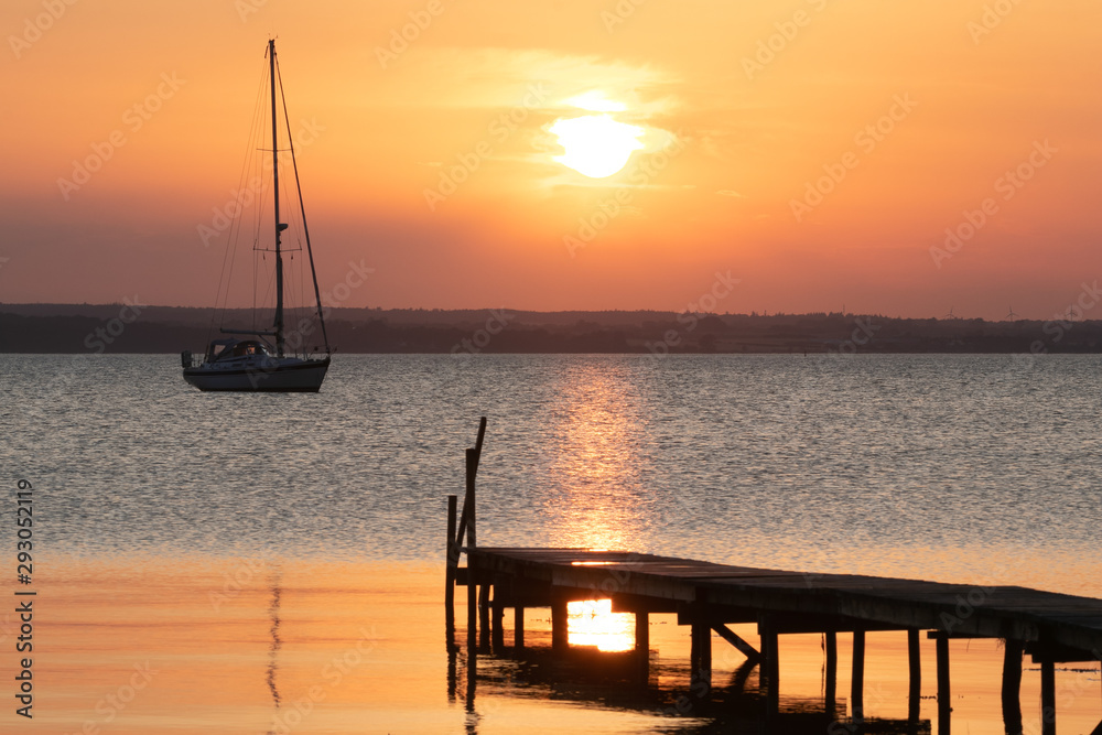 tranquil sunset seascape with sail boat and jetty