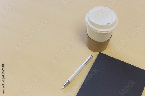 Take away Paper cup coffee with a notebook and pens on the table . photo