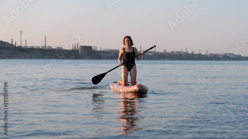 Girl rides on a surfboard with a paddle in sunset light © fitmen