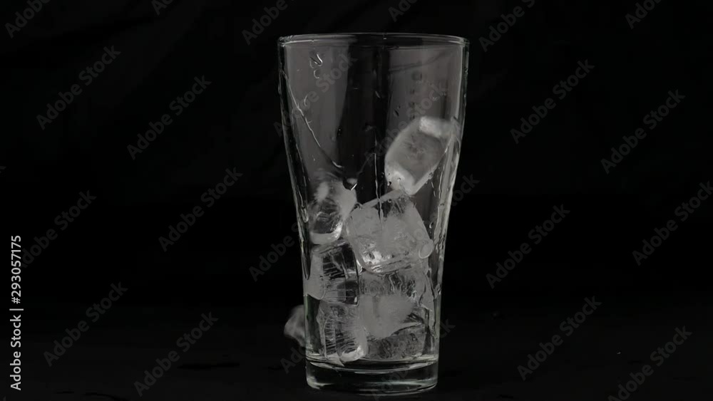 Ice cubes falling in the empty glass on black background, front view with details.