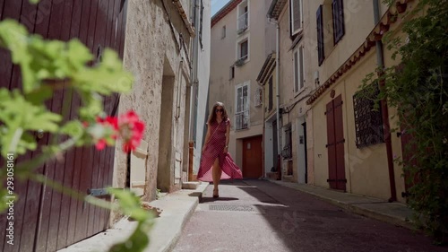 Girl with long hair in romantic red summer dress and sunglasses walks through the narrow medieval Parisian streets in the city of Antibes. Distant plan