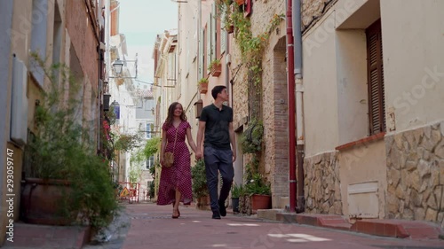 Lovers couple walking holding hands and smiling in old town of Antibes, France. Distant plan