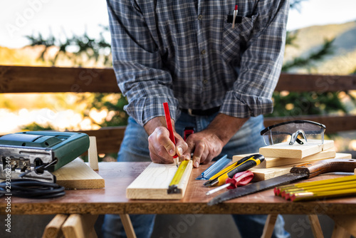 Adult craftsman carpenter with pencil and ruler tracing the cutting line on a wooden table. Housework do it yourself. Stock photography.