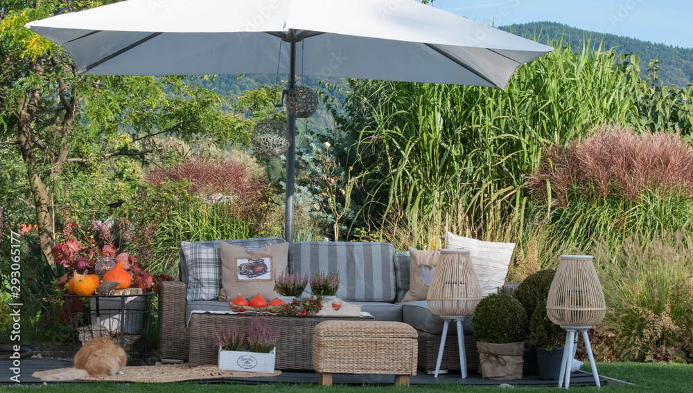 Naklejka premium Wypoczynek w pięknym ogrodzie wśród traw i roślin na tarasi z parasolem i meblami ogrodowymi. Strefa wypoczynku 