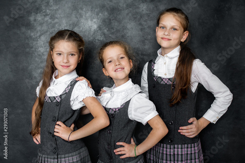 Portrait of three schoolgirls in school uniform on a gray background