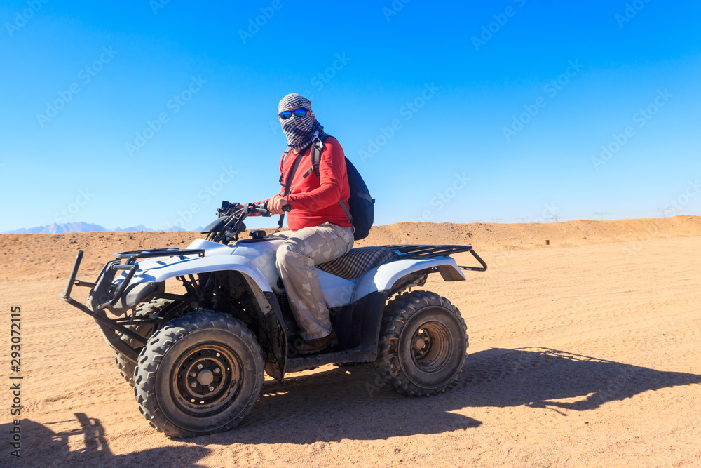 Young man in safari trip through egyptian desert driving ATV. Quad bikes safari in the desert near Hurghada, Egypt Young man in safari trip through egyptian desert driving ATV. Quad bikes safari in the desert near Hurghada, Egypt