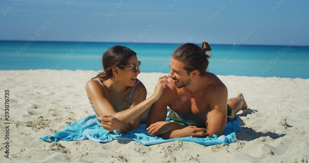 A happy young couple is having fun to apply a sunscreen or sun tanning lotion to take care of their skin during a vacation on a beach. A happy young couple is having fun to apply a sunscreen or sun tanning lotion to take care of their skin during a vacation on a beach.
