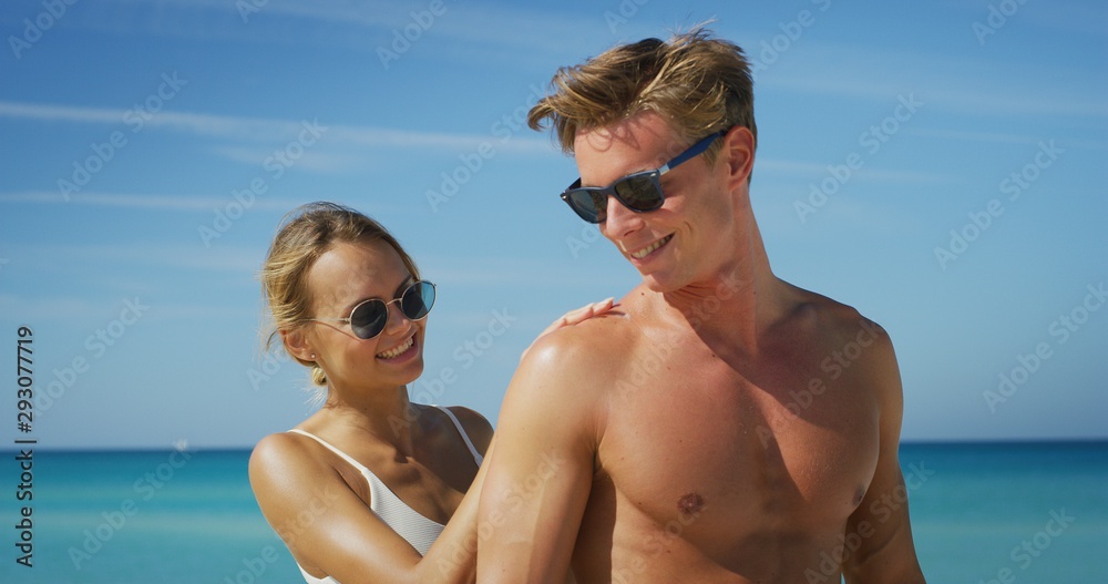 A happy young couple is having fun to apply a sunscreen or sun tanning lotion to take care of their skin during a vacation on a beach. A happy young couple is having fun to apply a sunscreen or sun tanning lotion to take care of their skin during a vacation on a beach.